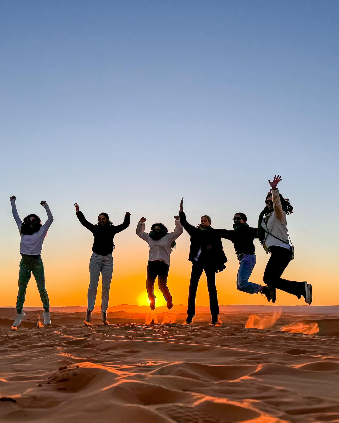 Silhouette of a camel caravan crossing a Sahara dune at sunset.